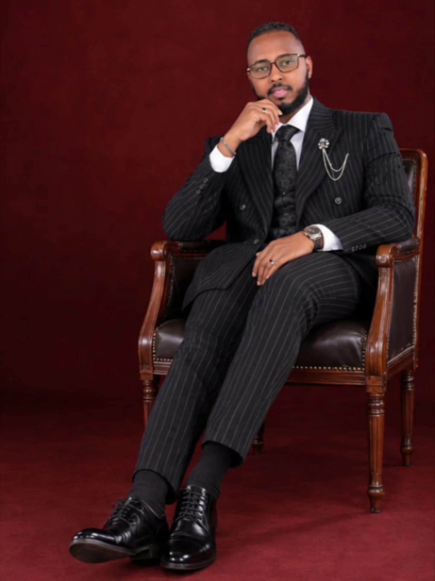 Seated portrait wearing a black pinstripe three-piece suit